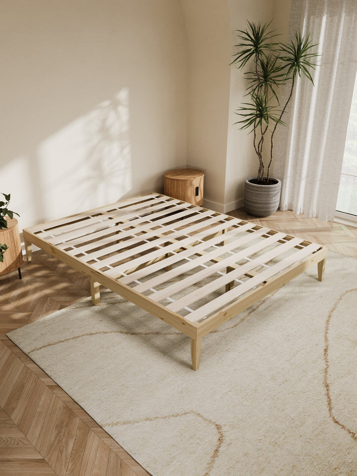 Contemporary bedroom featuring the Ventura Classic Wooden Bed Base in a clean, minimalist design. The natural light highlights the bed's sturdy construction and elegant finish, perfect for those looking to enhance their home with durable, stylish furniture. Paired with soft beige bedding and a lush view from the window, this bed base is ideal for modern décor enthusiasts.
