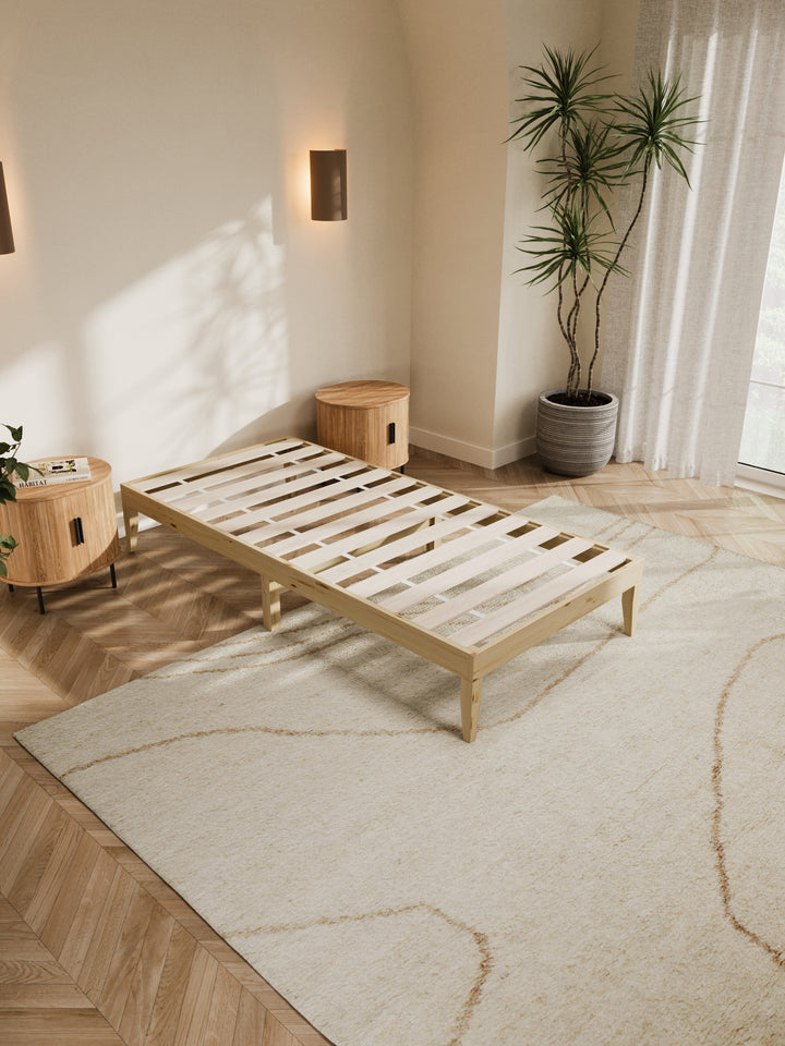 Contemporary bedroom featuring the Ventura Classic Wooden Bed Base in a clean, minimalist design. The natural light highlights the bed's sturdy construction and elegant finish, perfect for those looking to enhance their home with durable, stylish furniture. Paired with soft beige bedding and a lush view from the window, this bed base is ideal for modern décor enthusiasts.